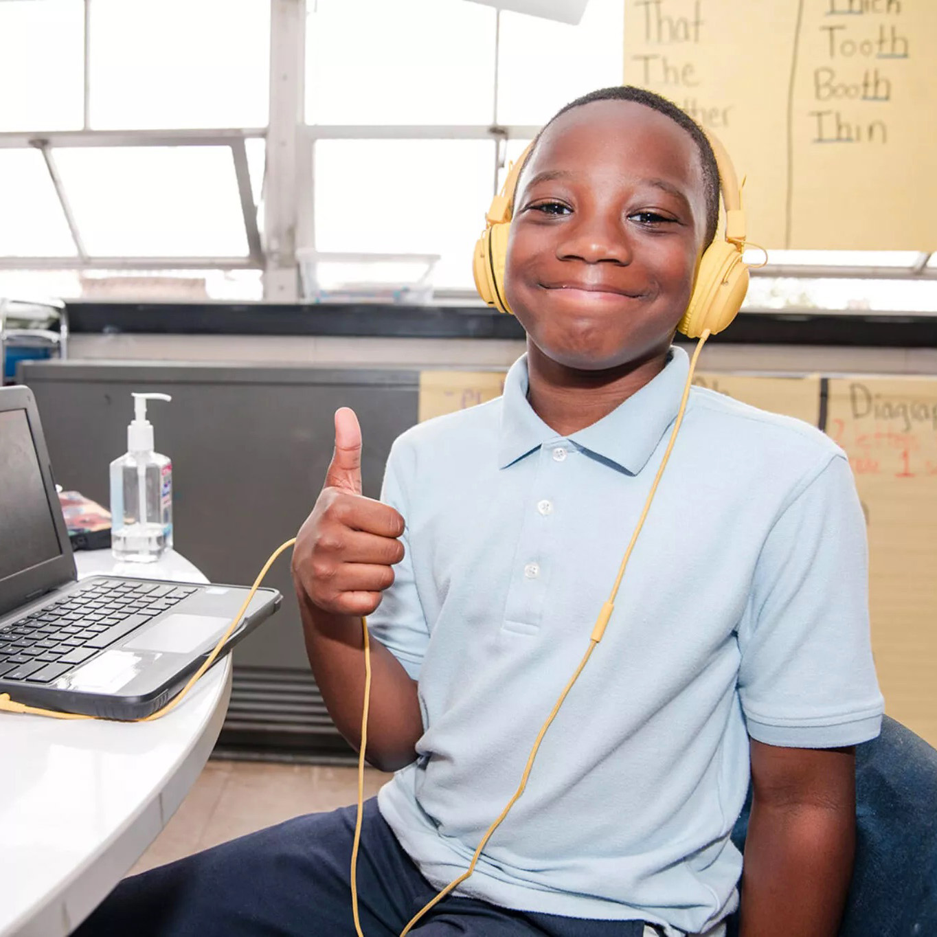 A Morton McMichael School student wearing headphones gives a thumbs up while using a laptop for classroom learning.